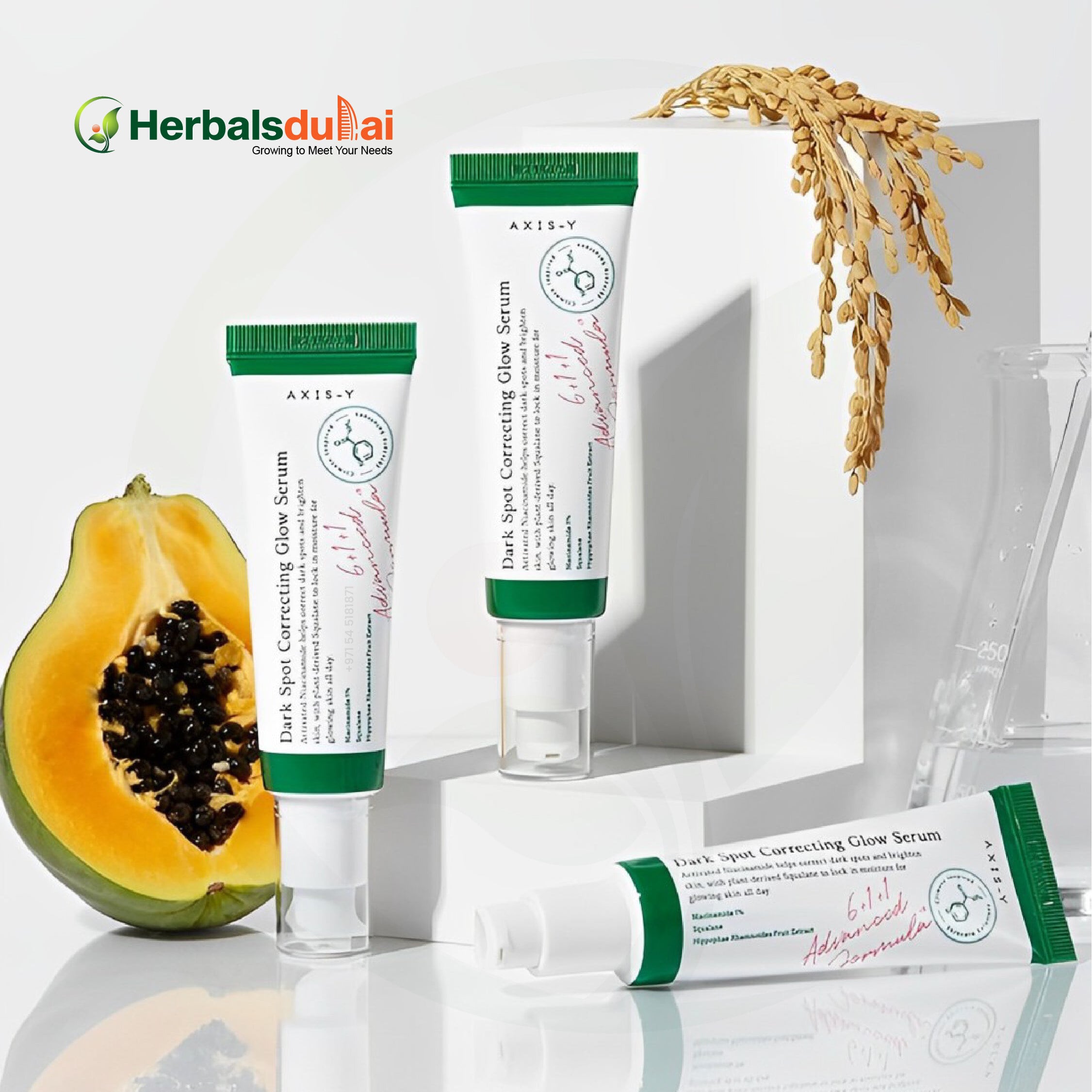 Tubes of AXIS-Y Dark Spot Correcting Glow Serum displayed with a sliced papaya and grains for an aesthetic presentation, under the Herbals Dubai branding.