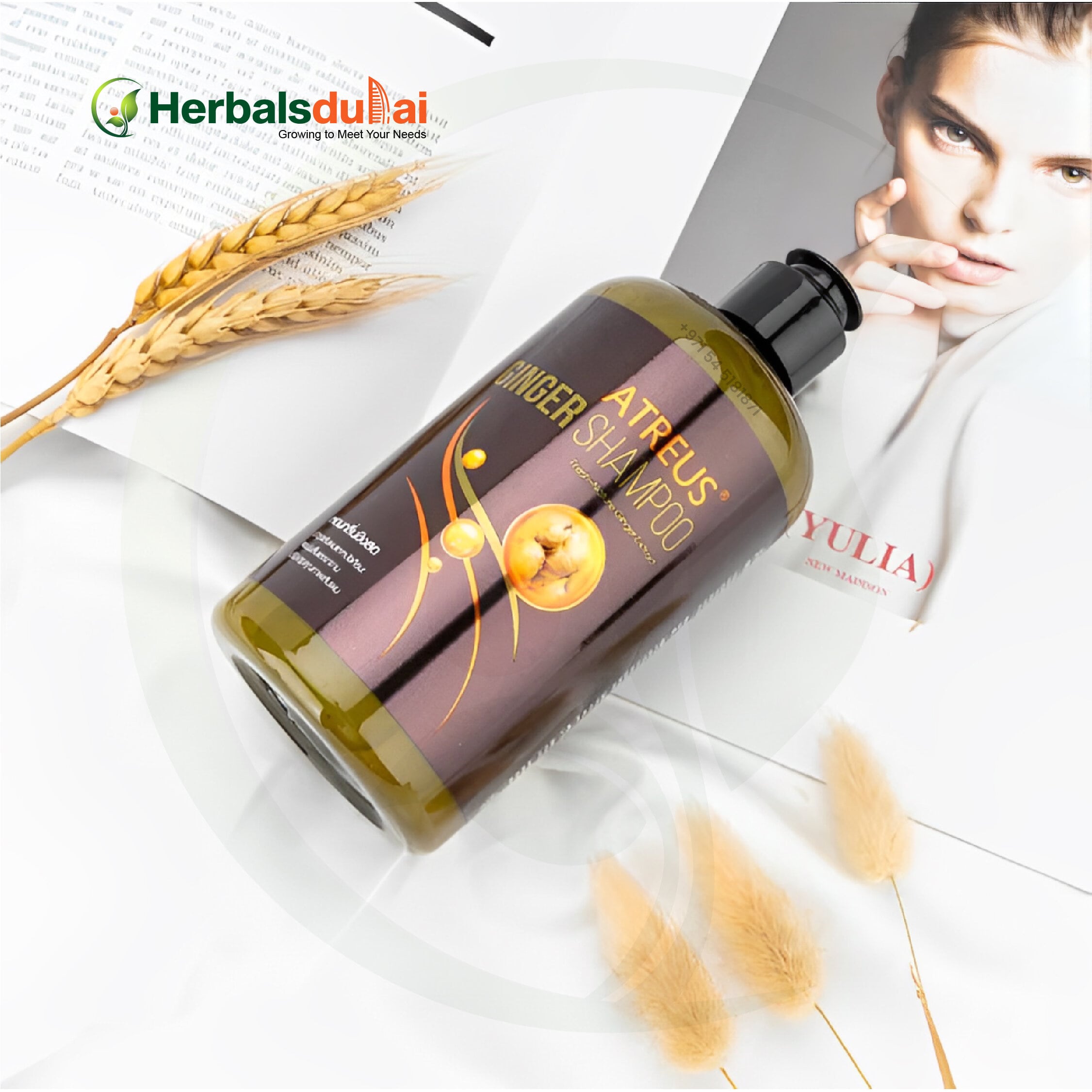 A bottle of Atreus Ginger Shampoo placed on a magazine with decorative wheat stalks and soft fluffy elements, showcasing its herbal beauty product appeal.