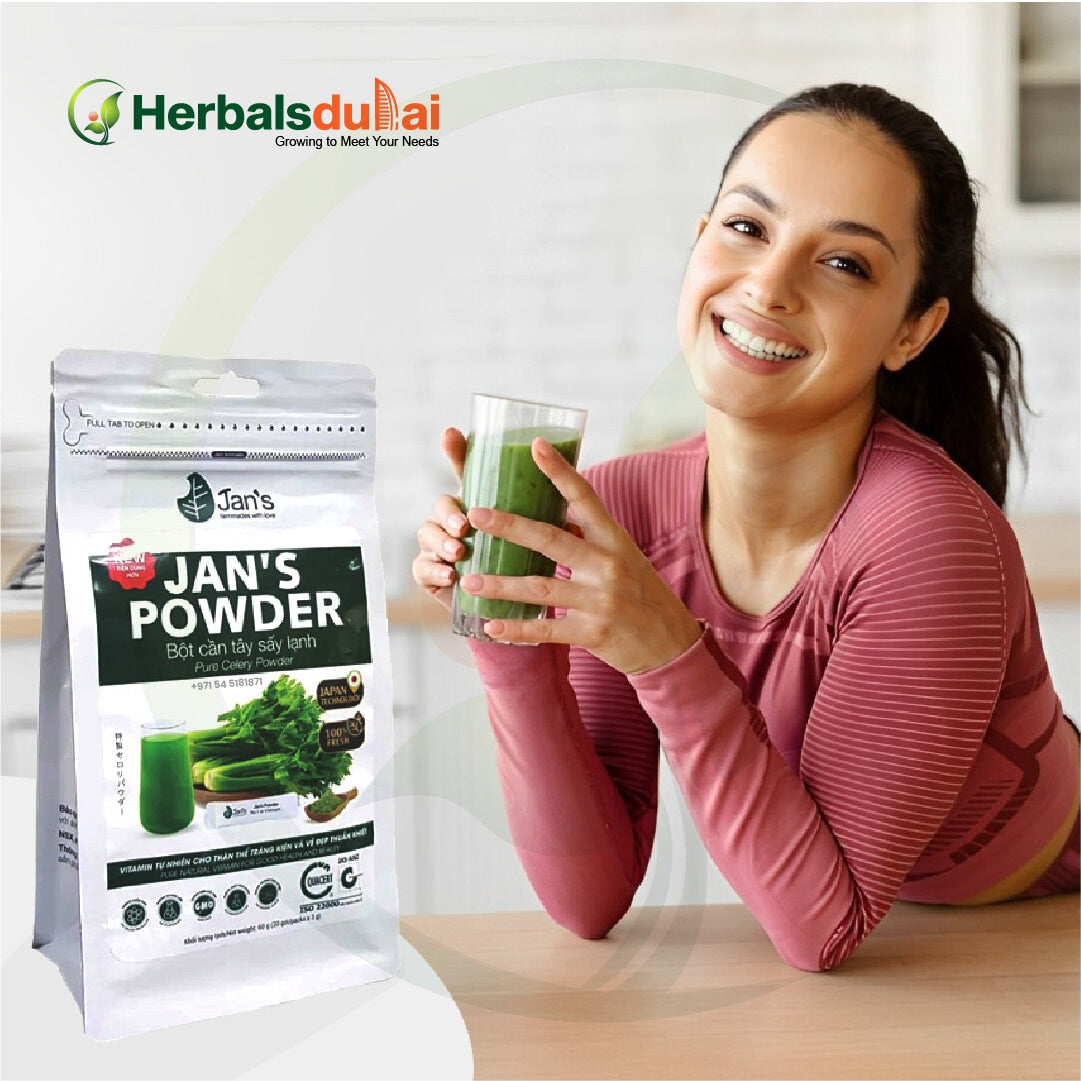 Smiling woman in a pink top holding a glass of green smoothie, with a package of Jan's Powder celery powder from Herbals Dubai displayed beside her.