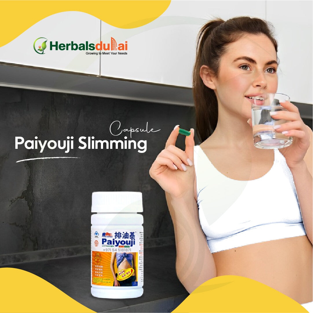 A woman in a sports outfit holding a glass of water and a capsule next to a container of Paiyouji Slimming capsules on a kitchen counter, with the Herbals Dubai logo in the background.