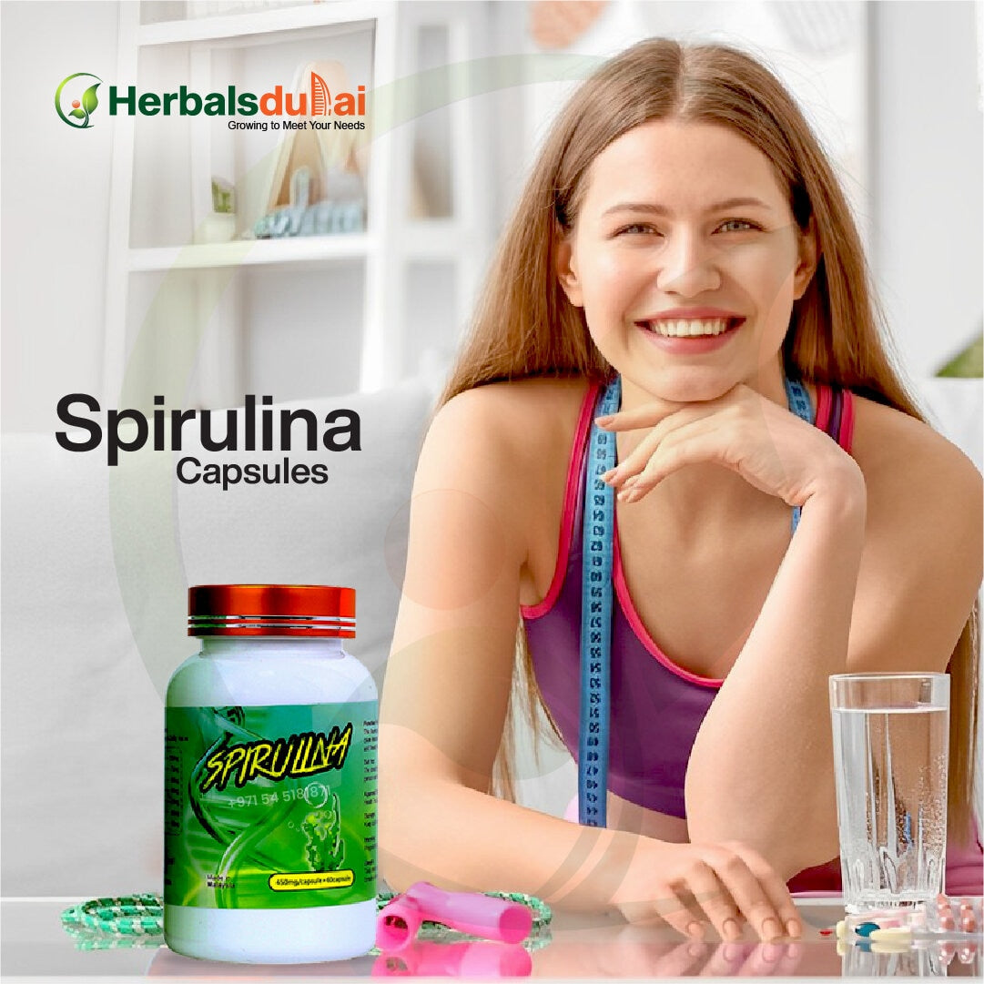 A smiling woman with a fitness theme, featuring a bottle of spirulina capsules from Herbals Dubai, a measuring tape around her neck, a glass of water, and exercise hand grips on a table.